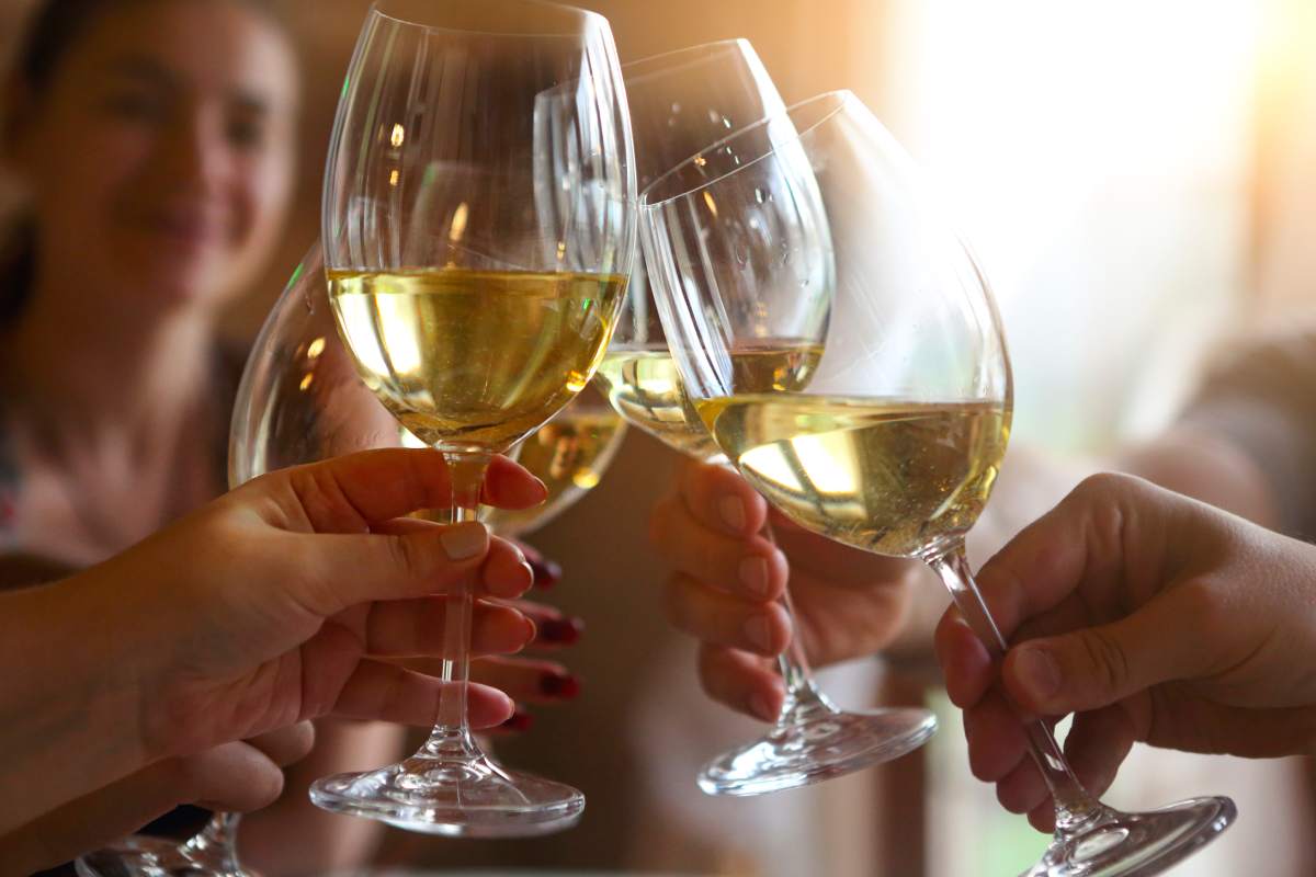 Group of friends enjoying evening drinks. Close up of toast with white wine