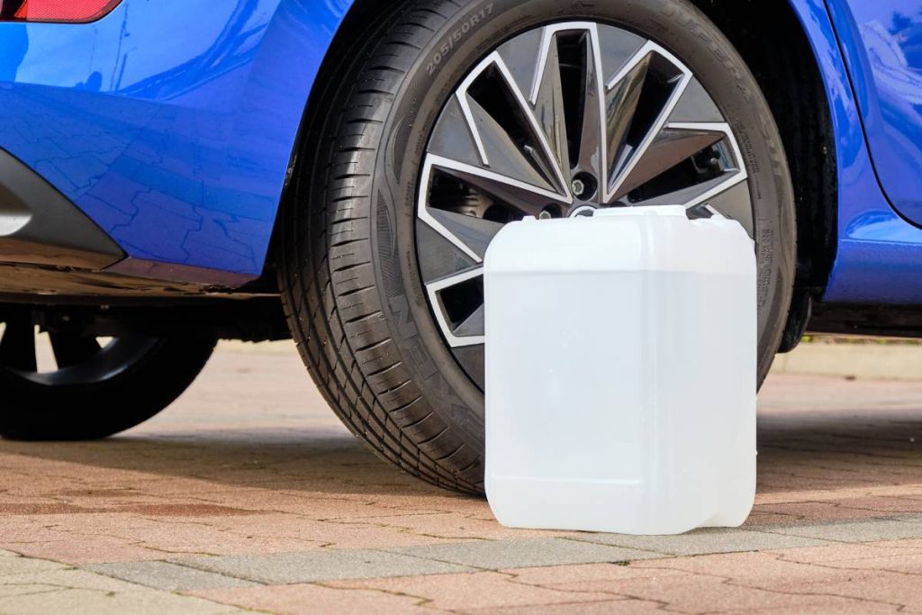 A white canister with a diesel exhaust fluid DEF for reduction of air pollution standing near a blue car